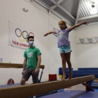Girl and masked instructor on the balance beam